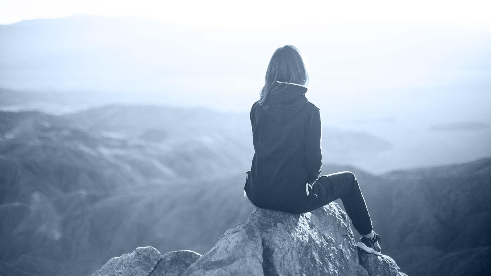 Junge Frau auf der Spitze eines Berges blickt in die Ferne